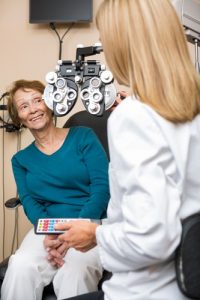 Happy senior woman undergoing eye checkup while optometrist adjusting phoropter in store